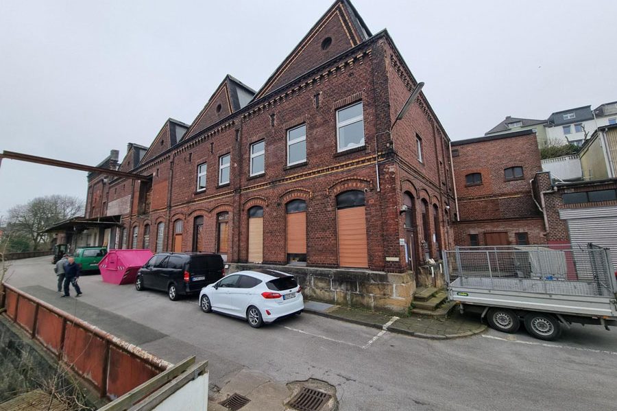 Mehrstöckiges Wohngebäude mit grünem Rasen und Bäumen im Vordergrund.